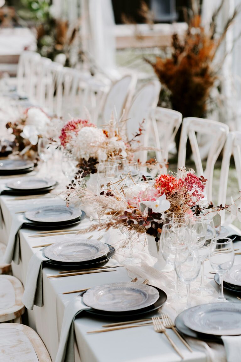 long table laid with black and grey plates and read and pink flowers