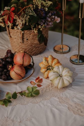 Rustic autumn table setting with gourds, pomegranates, and flower arrangement.